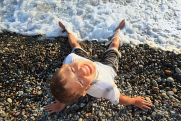 sitting teenager boy looking upwards on stone seacoast, wets fee