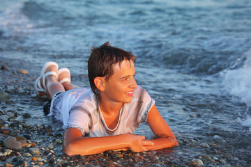 teenager boy  in wet clothes lying on stones on seacoast