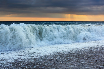 Sea coast with waves, wide angle; sun appeared through clouds