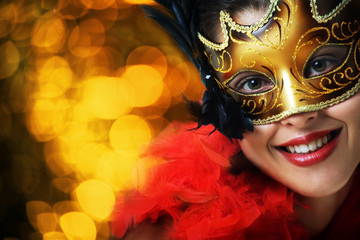 Beautiful young woman in carnival mask over gold background