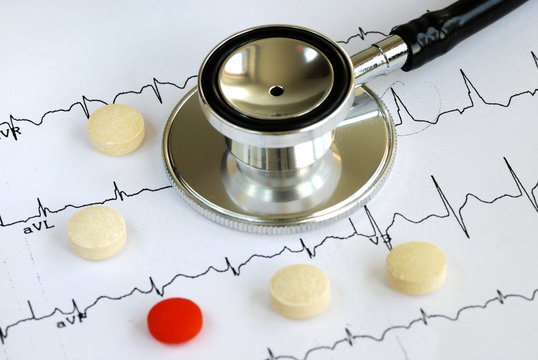 A stethoscope on the top of the EKG chart with pills