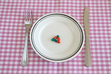 Capsules on a plate with a knife and fork, signifying dieting.