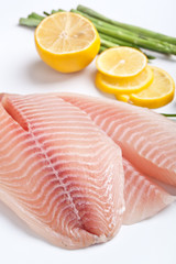 raw filleted tilapia with asparagus, parsley and lemon on white