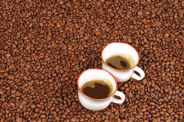 Two cups of coffee an a background of roasted coffee beans