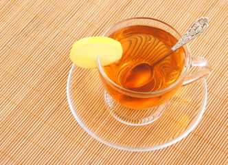 Glass cup of tea with spoon and lemon on wooden background