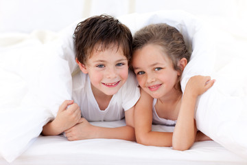 Delighted siblings lying in the bed at home
