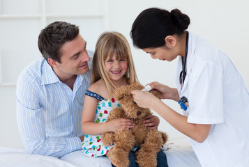 Smiling patient examining a teddy bear with a doctor