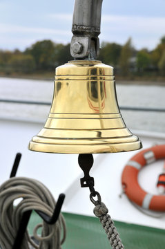 Goldene Schiffsglocke an Bord, im Hintergrund Rettungsring