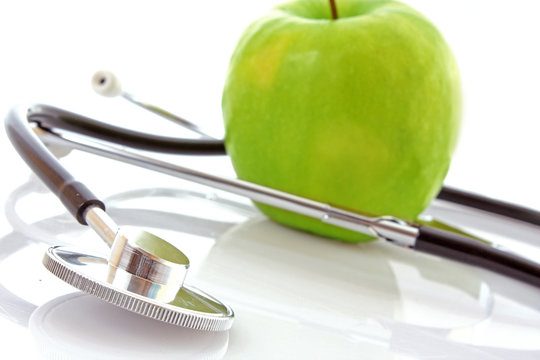 Stethoscope and green apple on white background