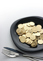 Golden coins on plate with fork and knife