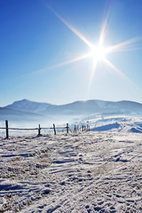 Wooden fence in snow covered mountains under blue sky and shiny