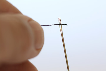 Close up of a thread being threaded through a needle hole.