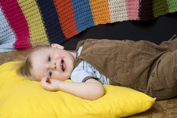 little cute smiling blond boy lying on big yellow  pillow