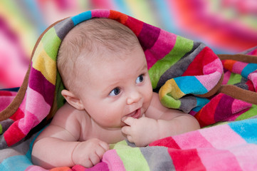 Baby with finger in mouth comes out from a colorful blanket