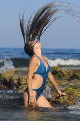 Young girl in a swimsuit is making waves of water with her hair