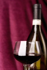 red wine in glass and bottle on a claret background