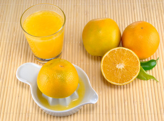Fresh orange juice on a table mat with squeezer and oranges