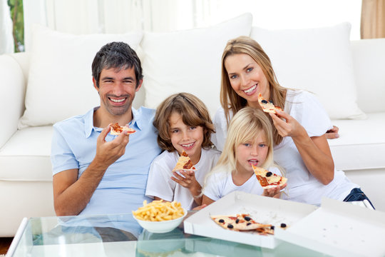 Smiling family eating a pizza sitting on the floor