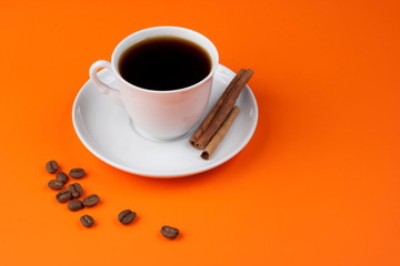 Black coffee cup on orange with cinnamon and beans