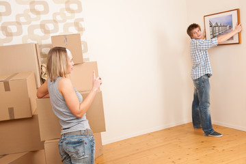 Fototapeta na wymiar Moving house: Couple hanging picture on wall