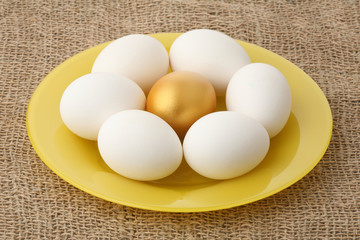 Gold egg among white on a yellow plate