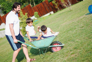 Dad in white driving boys on the wheelbarrow