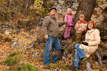 Mother, children and grandfather in autumnal forest near tree