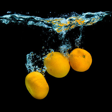 Fresh tangerines dropped into water with bubbles on black