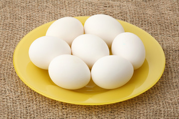 Seven white eggs on a yellow plate
