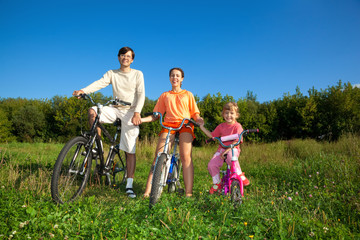 Fototapeta na wymiar Parents with daughter on bicycles in park a sunny day.