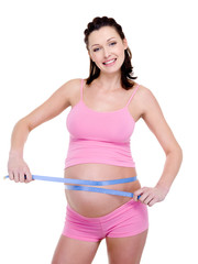 Pregnant woman measures her tummy on a white