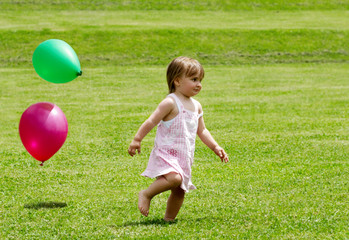 The little girl running on a grass with balloons