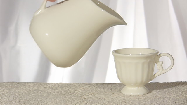 Milk pouring from the pot into empty cup