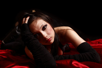 young woman in black laying on a red satin sheet