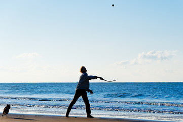 Man throwing ball for dog at Zandvoort in The Netherlands - obrazy, fototapety, plakaty