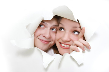young couple peeping through hole in white paper