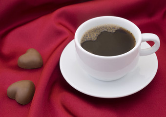 Cup of coffee and chocolate hearts on red satin