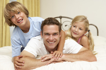Obraz premium Father And Children Relaxing On Bed At Home