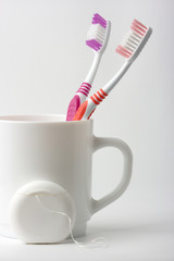 Two toothbrushes in a cup and dental floss - common toiletries