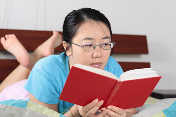 An Asian woman reading a book on a bed