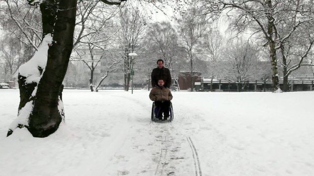junger Rollstuhlfahrer mit Pfleger im Park