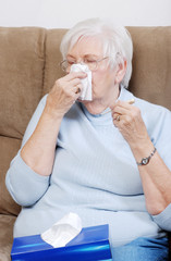 sick senior with thermometer blowing her nose