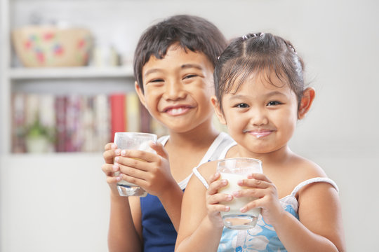 Two Little Girl And Boy Each Holding Glass Of Milk