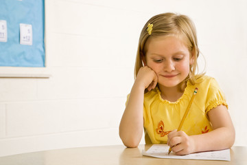 Naklejka premium Young Girl Smiling in Classroom Writing on Paper