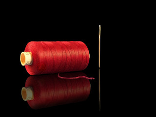 Nadel und roter Faden mit Spiegelung vor schwarzem Hintergrund