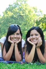 Two smiling sisters lying outdoors in grass