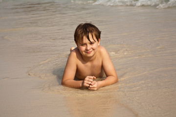 Fototapeta na wymiar boy is lying at the beach and enjoying the water and the sand
