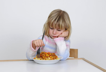 Kleines Maedchen stochert schlecht gelaunt im Essen herum.