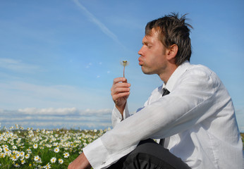 A businessman blowing dandelion on the meadow,