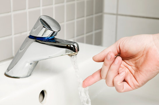 Frauenhand pr&uuml;ft Wassertemperatur am Wasserhahn